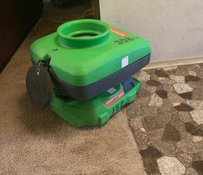 Green air mover sitting on carpet and tile. 