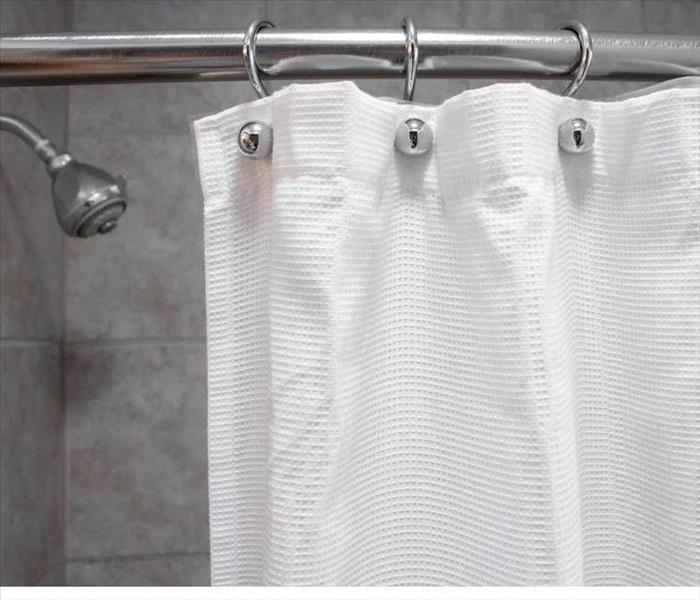 A white shower curtain in an empty shower with water OFF medium shot